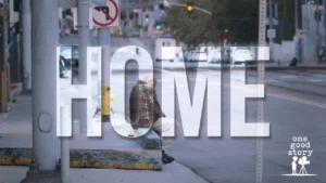 A man walking along a city street past traffic and parked cars, under the film title Home
