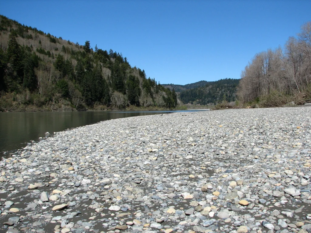 The Klamath River running past a wide gravel bar below a steep forested hillside.