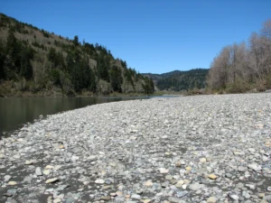 The Klamath River running past a wide gravel bar below a steep forested hillside.