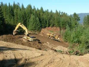 A tracked excavator and a bulldozer removing the fill of an old logging road on a forested hillside in the Greater Mill Creek watershed, Redwood National and State Parks.