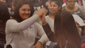 A high school student wearing a blue Who I Am Makes a Difference ribbon high-fives a classmate at a school assembly