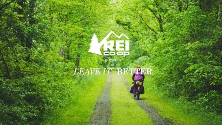 Opening frame of Leave It Better, with the REI Co-op and film title over a cyclist on a green forest path